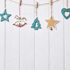 Wall Mural - Christmas card with place for your text. Wooden figures of green color in the form of stars, Christmas tree, hearts, horses hanging on clothespins on a rope on a white background of wooden boards