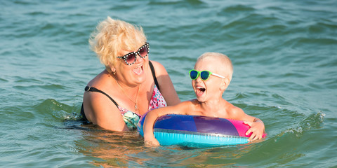 Grandmother and little grandson swim in the sea.The baby in the bouncy multicolored circle.Summer vacation.