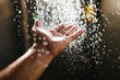 A man's hand in a spray of water in the sunlight against a dark background. Water as a symbol of purity and life
