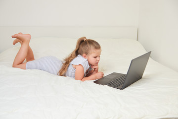 Wall Mural - Little girl with laptop lying on bed