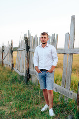 Young handsome man in a white shirt and jeans shorts outdoors