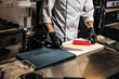 Close-up photo of a cook in uniform and gloves preparing sushi on cutting board in the kitchen.