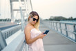 © phoenix021 - Elegant young woman looking at smartphone while standing on the bridge