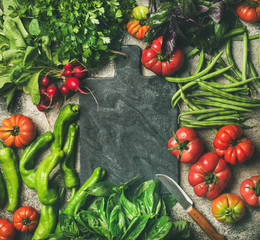 Wall Mural - Healthy seasonal food cooking background. Flat-lay of fresh vegetables and greens over grey concrete background, black board in center, top view, copy space. Clean eating, vegan food preparation