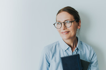 Beautiful old woman in casual clothes and glasses holding books.Portrait of mature woman with book looking at camera