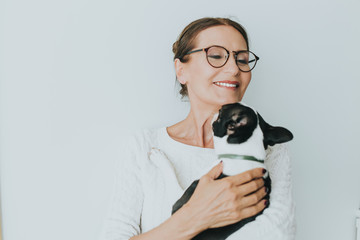 Close up of Happy looking mature woman is enjoying at home with her pet dog.A portrait of a happy mature woman with her boston terrier puppy. Positive emotions.woman laughing and playing with puppy 