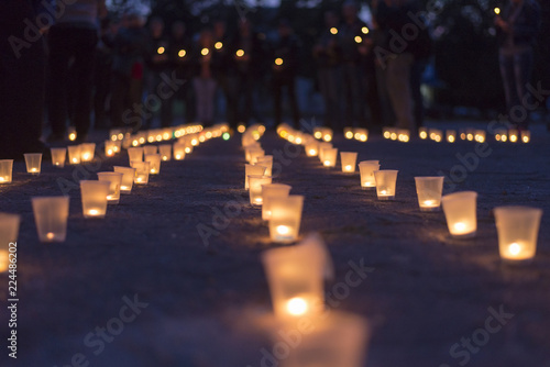 Cuadros en Lienzo A group of candles burning in street and people holding candles in the background