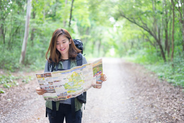 Hipster Asian young girl with backpack enjoying forest on mountain.Tourist traveler with trendy look searching direction on location map , Greenfield. Hiker looking sunlight in trip in the countryside