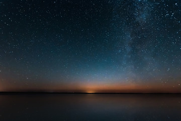 Blue Night Starry Sky With Milky Way Galaxy Above Lake And Russian Village. Night Glowing Stars