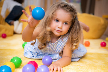 adorable caucasian kid playing on carpet with colored balls in kindergarten