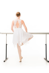 Wall Mural - back view of ballerina in tutu and pointe shoes practicing at ballet barre stand isolated on white background