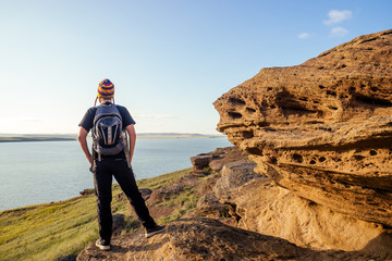 man travel blogger in a funny hat from Nepal mountain Hiker with backpack hike walking on orange huge stones landscape lake and hills