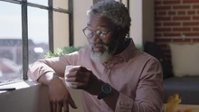 Mature African American Man Drinking Coffee At Home Enjoying Relaxed Morning Looking Out Window Planning Ahead Thinking Successful Black Businessman Smiling Wearing Glasses