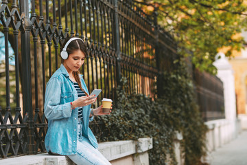 Wall Mural - Young woman listens to music via headphones and smartphone in the city