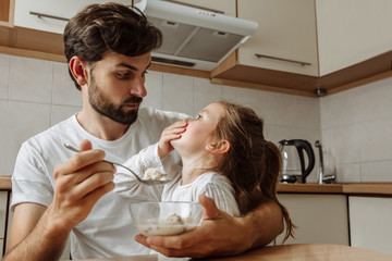 Family. Food. Parenthood. Dad is feeding his little daughter who is refusing to eat. In the kitchen at home