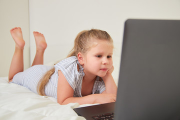 Wall Mural - Little girl with laptop lying on bed