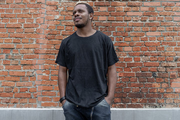 Close up of dark-skinned man in black blank T-shirt on bricked background.