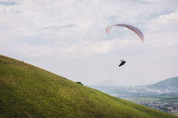 A white-orange paraglider flies over the mountainous terrain