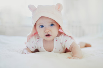 Adorable baby girl in pink hoody crawling on bed