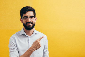 Wall Mural - Smiling bearded man pointing on side on colorful yellow background.