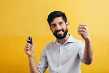 Sticker - Portrait of young man smiling and holding car keys. Isolated yellow background