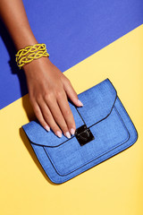 Female hand with bracelets and handbag on colorful background