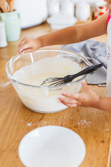 3 years cute girl preparing dough for pancakes at the kitchen.