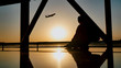 Silhouette of a tourist guy watching the take-off of the plane sitting at the airport window at sunset in the evening. Travel concept, people in the airport.