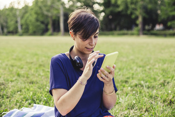 Wall Mural - Young adult woman using a mobile phone at the public park in summer