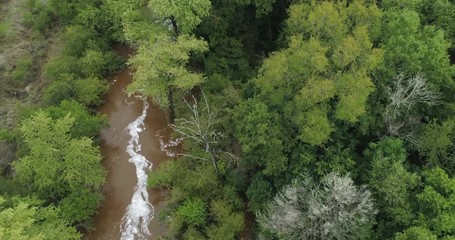 Aerial top to bottom and tilt up from a flooded river to the green landscape it flows through.  Located in Buda, Texas on the Onion Creek.