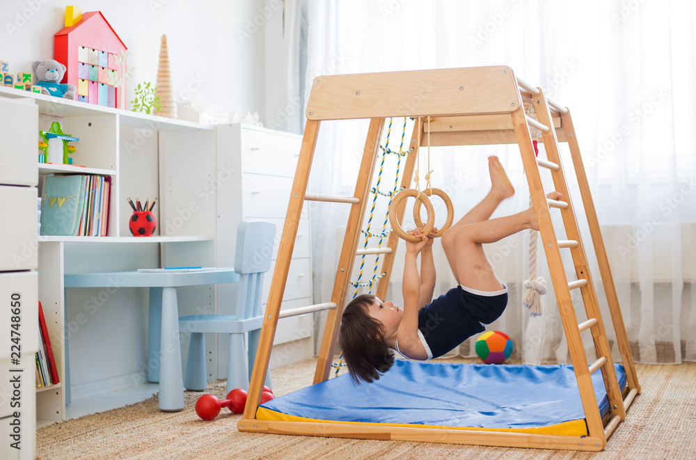 little girl performs gymnastic exercises on a wooden home sports ...