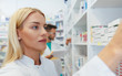 © Karanov images - Serious woman pharmacist reaching for a medications among shelves at pharmacy drugstore
