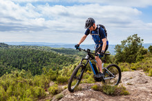 Male Mountain Biker Balancing His Ebike On A Rock, Nice Landscape In The Background