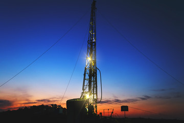 Wall Mural - drilling rig drills a well for the extraction of drinking water at sunset under a beautiful sky for drinking people