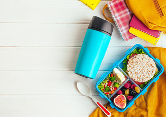 Lunch box on white wooden background near thermo mug and school accessories