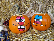 Pair Of Autumn Pumpkins With Fun Painted Faces On Hay Bale