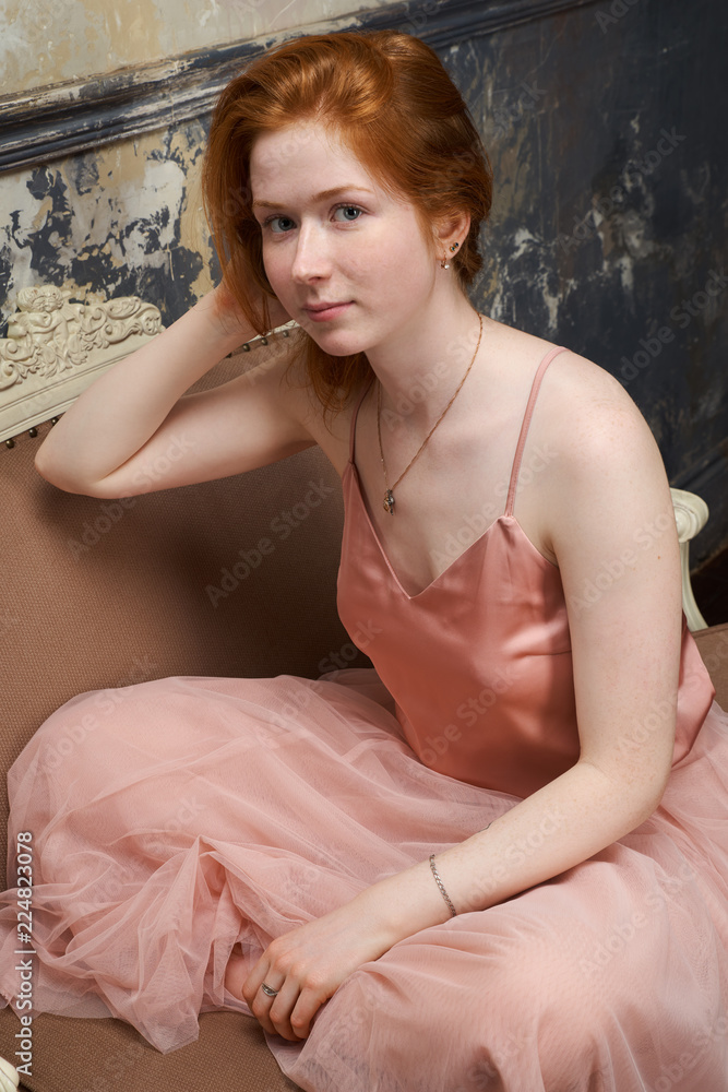 young attractive redhead woman in pink dress posing for portrait sitting on  couch cross-legged in Lotus position Stock Photo | Adobe Stock