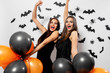 © Leika production - Gorgeous brunette woman in black dress holds black and orange balloons on a white background with black bats and spiders. Halloween