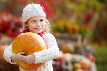 Cute little girl playing with pumpkins in autumn park. Autumn activities for children. Halloween and Thanksgiving time fun for family.