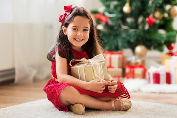 christmas, holidays and childhood concept - happy girl with gift box at home