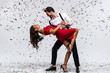 Rumba time. Full length of young beautiful couple dancing while standing against white background with confetti 