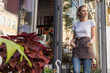 © LIGHTFIELD STUDIOS - attractive florist in apron standing near flower shop and looking away