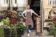 © LIGHTFIELD STUDIOS - smiling handsome flower shop owner standing on stairs and leaning on open sign