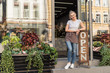 © LIGHTFIELD STUDIOS - smiling attractive florist standing on stairs of flower shop and leaning on open sign