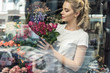 © LIGHTFIELD STUDIOS - view through window of attractive florist holding bouquet of burgundy roses in flower shop