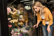 © LIGHTFIELD STUDIOS - attractive girl looking at showcase with flowers at store