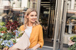 © LIGHTFIELD STUDIOS - portrait of attractive smiling girl going out from flower shop with wrapped bouquet and looking away