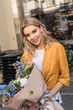 © LIGHTFIELD STUDIOS - attractive girl standing with wrapped bouquet near flower shop and looking at camera