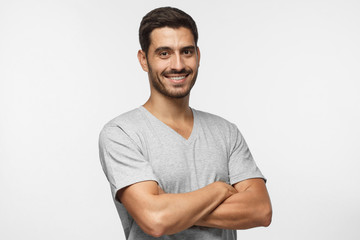 Wall Mural - Portrait of attractive young sporty man in gray t-shirt standing with crossed arms isolated on grey background