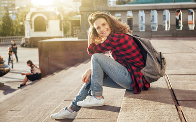 Beautiful young happy smiling woman against the background of a European city in the sun at sunset, student and traveler, vacation in the city